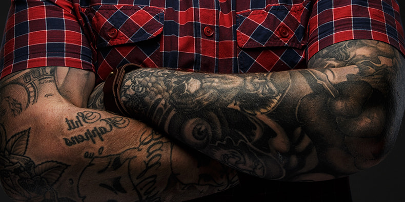 Muškarac u košulji s rukom u džepu i tetovažom na podlaktici 
